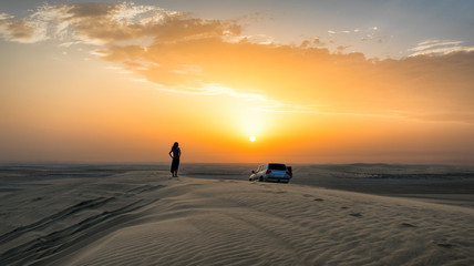 Frau mit Geländewagen auf einer Düne in der Wüste von Katar bei Sonnenuntergang