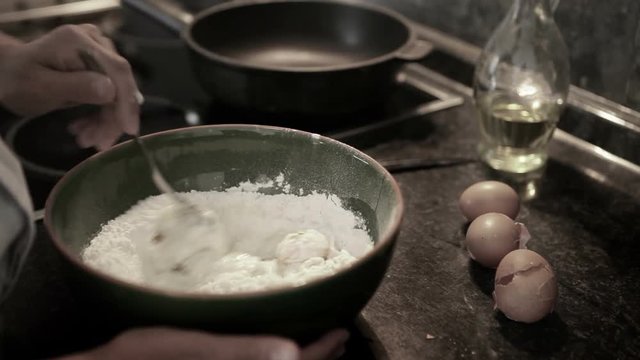 Muted real-time footage of a cook mixing eggs with flour in a bowl to make dough
