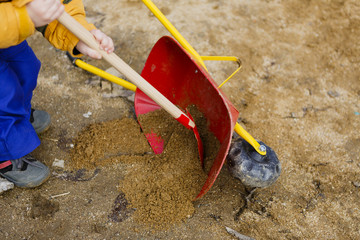 child play with sand, red shovel and small cute barrow