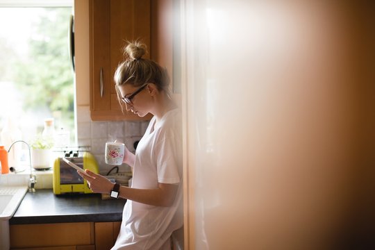 Woman using digital tablet while having coffee in kitchen