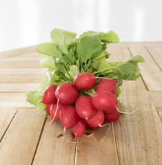 A bunch of fresh dirty radish lies on a light wooden table
