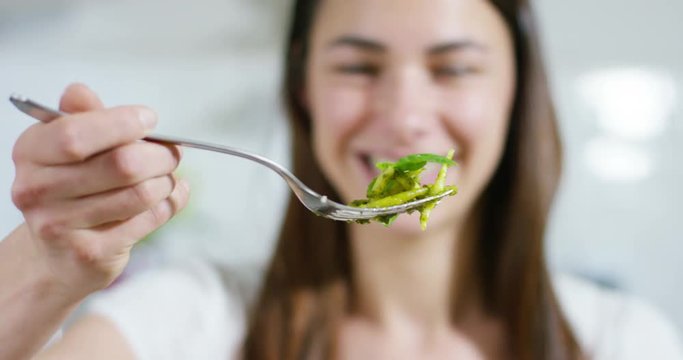 A beautiful woman lifts her fork with pasta al pesto, typical Italian dish, smiles and happy to eat healthy and tasty food. Concept: Italian spirit, food, healthy eating