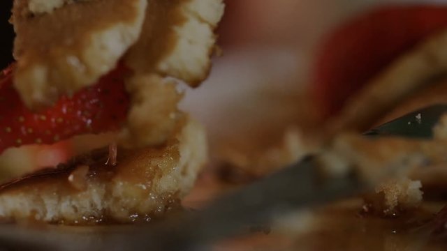 Close up of pancakes in maple syrup with strawberries being eaten