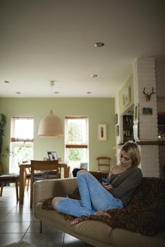 Woman sitting and using mobile phone on couch in living room