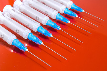 Hypodermic syringe. Syringes with blue needles on a red background. Medical Injectors
