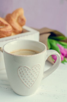 Cup of coffee with bouquet of pink tulips and croissants