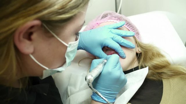 Cosmetologist is filling in the woman's lips with permanent makeup