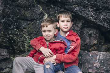 two sad boys hugging each other. Grieved brothers sit on the rocks