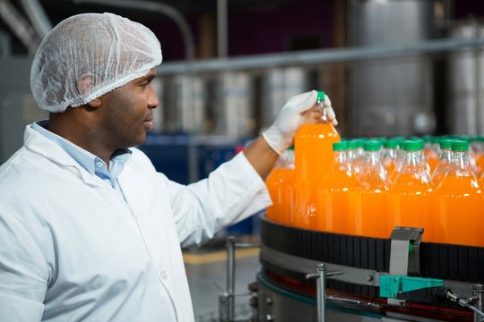 Male worker checking juice bottles in factory