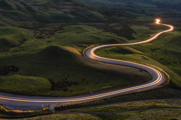 Winding curvy rural road with light trail from headlights leading through British countryside. - obrazy, fototapety, plakaty