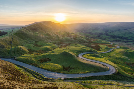 Sunset at Mam Tor in the Peak District with long winding road leading through valley.