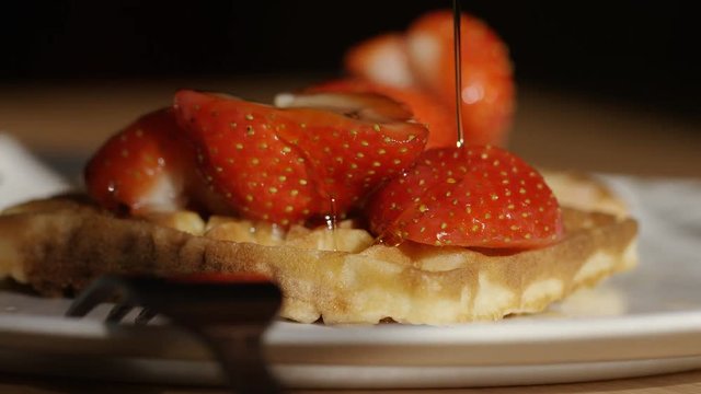 Waffles and strawberries being covered in maple syrup, in slow motion 