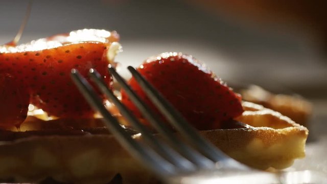 Maple syrup being drizzled over waffles and strawberries, in slow motion