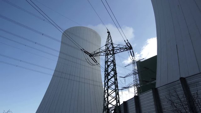 Wide angle shot of a large electrical pole in front of an industrial cooling tower used to cool the machinery an industrial power plant that generates electricity..