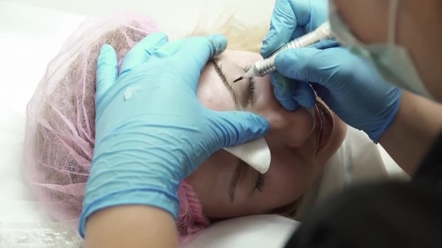 Closeup of beautician is making an eyebrow permanent makeup in salon