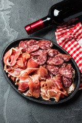 Plate of spanish jamon serrano and salami and bottle of red wine on slate background. Top view