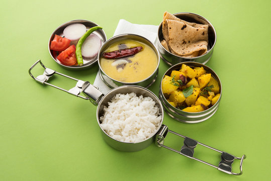 indian typical stainless steel lunch box or tiffin with north indian or maharashtrian food menu like chapati//roti, dal tadka, white rice and aloo / potato sabji / gobi or cauliflower sabji with salad
