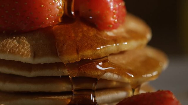 Maple syrup drizzled over stacked pancakes and strawberries