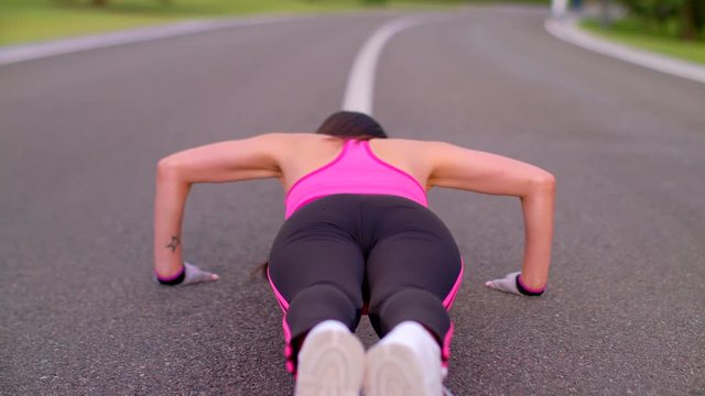 Push ups woman. Woman push ups on asphalt road. Back view of woman pushing on park road. Slim woman doing push up exercise. Fitness workout on park road. Sexy girl doing push ups outdoors