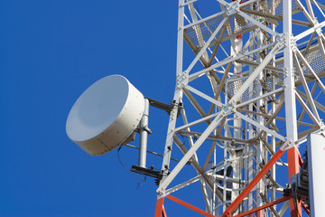 Mobile phone communication antenna tower with satellite dish on blue sky background