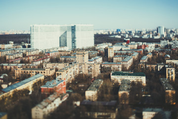 Fototapeta na wymiar Close-up tilt shift shooting from high point of residential district of metropolitan city on sunny spring day with multiple small houses and one huge in blurred distance, clear teal horizon and sky