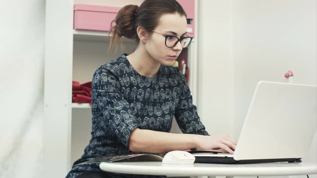 Beautiful young female showroom owner working using laptop computer and fashion magazine