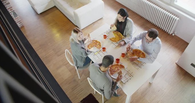 multiethnic group of friends people enjoy having lunch or dinner meal together eating pizza indoor in modern industrial house. 4k handheld slow motion top view overhead video shot