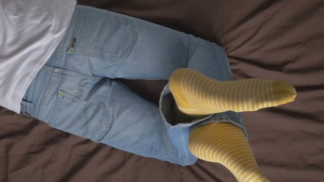 young man lying on the bed in jeans, a striped yellow socks . Lazy morning relaxing. Weekends are for relaxing in bed