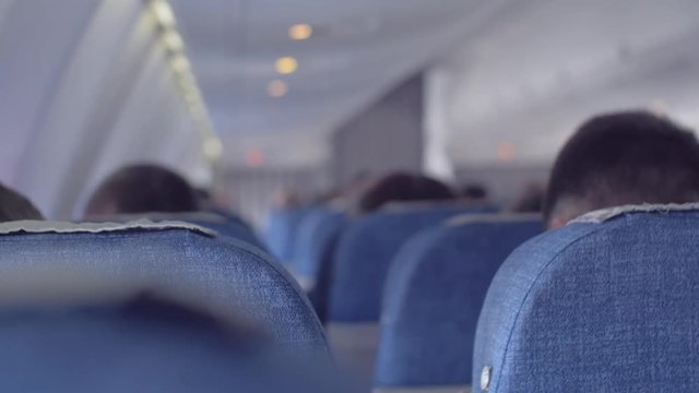 Passenger airplane saloon during the flight. Men and women are sitting in the passenger seats, the view from the back