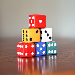 Tower of six colored dice with numbers from 1 to 6 on a wooden game table, soft background