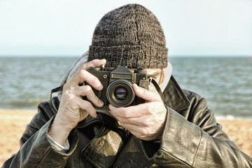 Photographer with retro photo camera on sea beach look at camera.Retro style toned image.