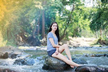 The girl is sitting at a waterfall and smiling happy