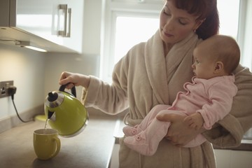 Loving mother carrying baby while making coffee