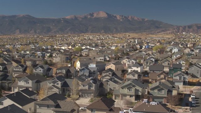 AERIAL CLOSE UP: Flying above luxury row houses in suburban town at the foothills of Rocky Mountains in Denver, Colorado. Modern wooden homes with backyards in beautiful neighborhood on sunny fall day