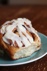 Cinnamon roll with white frosting on a blue plate with a wooden background 