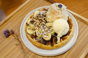 Waffles with banana and ice cream and syrup on wood table
