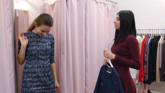 Surprised young woman trying on clothes in dressing room and discuss it with her friend