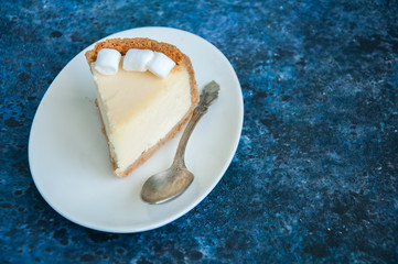 Slice of New York Cheesecake  style with marshmallows on white plate on blue background
