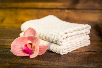 Spa or wellness set. White towels and pink flowers lily on brown wooden background. Selective focus. Place for text. Health concept.