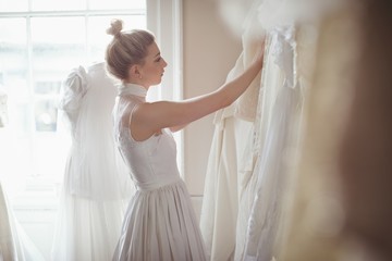 Young bride selecting wedding dress from clothes hanger