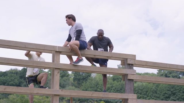  Competitors In Endurance Race, Teammates Helping Each Other Climbing Wall. 