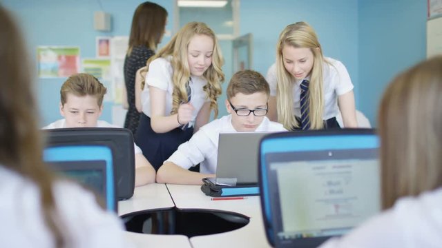  School children working on computers in class, young girls giving help to boy