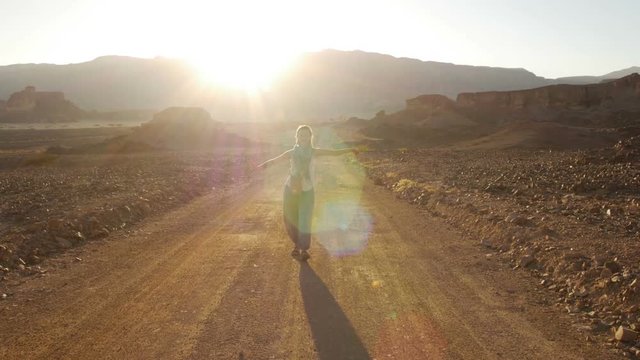 happy young woman walking in desert road on sunset with beautiful sun flare. Timna Park, Israel