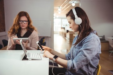 Two female executives using electronic devices at desk