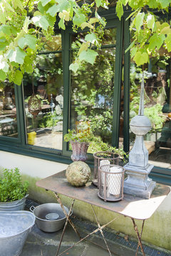 Terrace and reflection in a pane of the house with old iron table and pots surrounded by vineyards and greenery