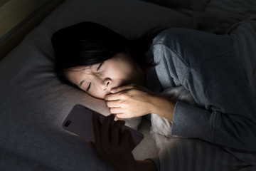 Fototapeta na wymiar Woman feeling tired and using mobile phone on bed