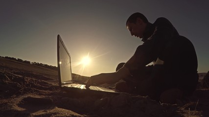 man businessman freelancer working behind laptop sitting on beach freelancing silhouette in the sun