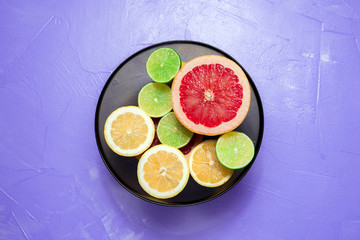Cut lemons, limes and grapefruit in glass bowl on lilac background. Top view