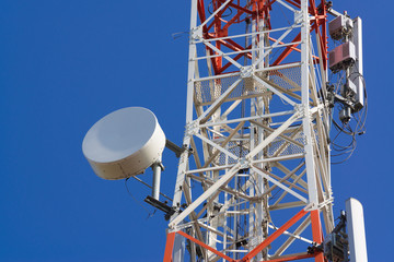 Mobile phone communication antenna tower with satellite dish on blue sky background