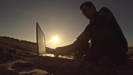 man businessman freelancer laptop working behind sitting on beach freelancing silhouette in the sun